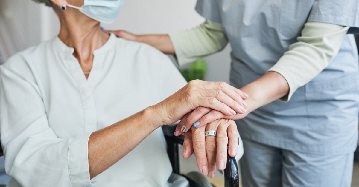 Nurse reassuring patient by placing her hand on her hand.