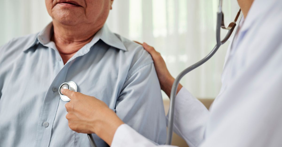 Close-up of female provider in white coat listening to breathe of senior man during his visit at hospital