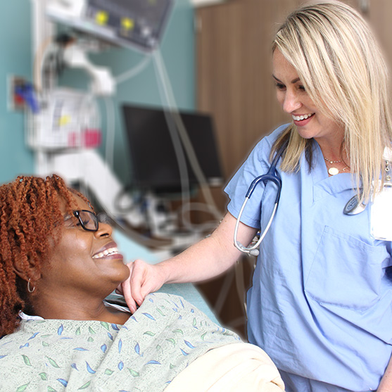 Nurse smiling with a patient who is in a hospital bed.