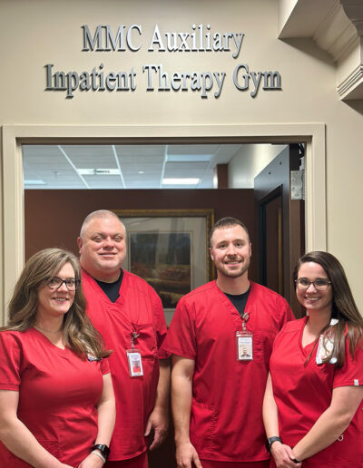 Physical therapists standing under a sign that says MMC Auxiliary Inpatient Therapy Gym.